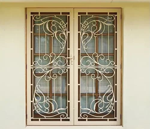 Pair of cream decorative cast security screen doors with a scroll pattern over timber windows