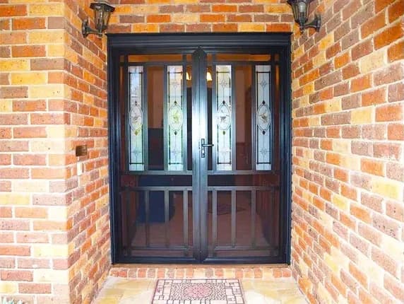 Black double decorative security doors with leadlight panels on a brick home entry