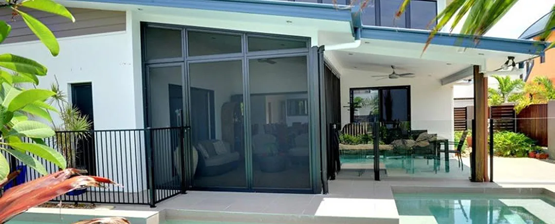 Poolside patio of a modern rendered home enclosed with dark security screens and framed by tropical plants