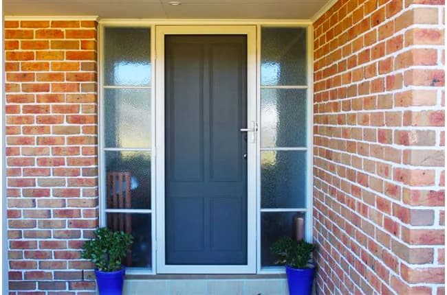 Hinged security screen door fitted over a grey front door on a brick home entry