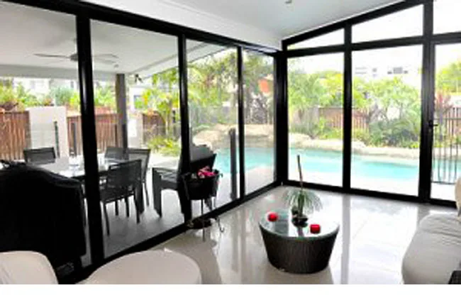 Open plan living room looking through black-framed security screen doors to a pool and palms